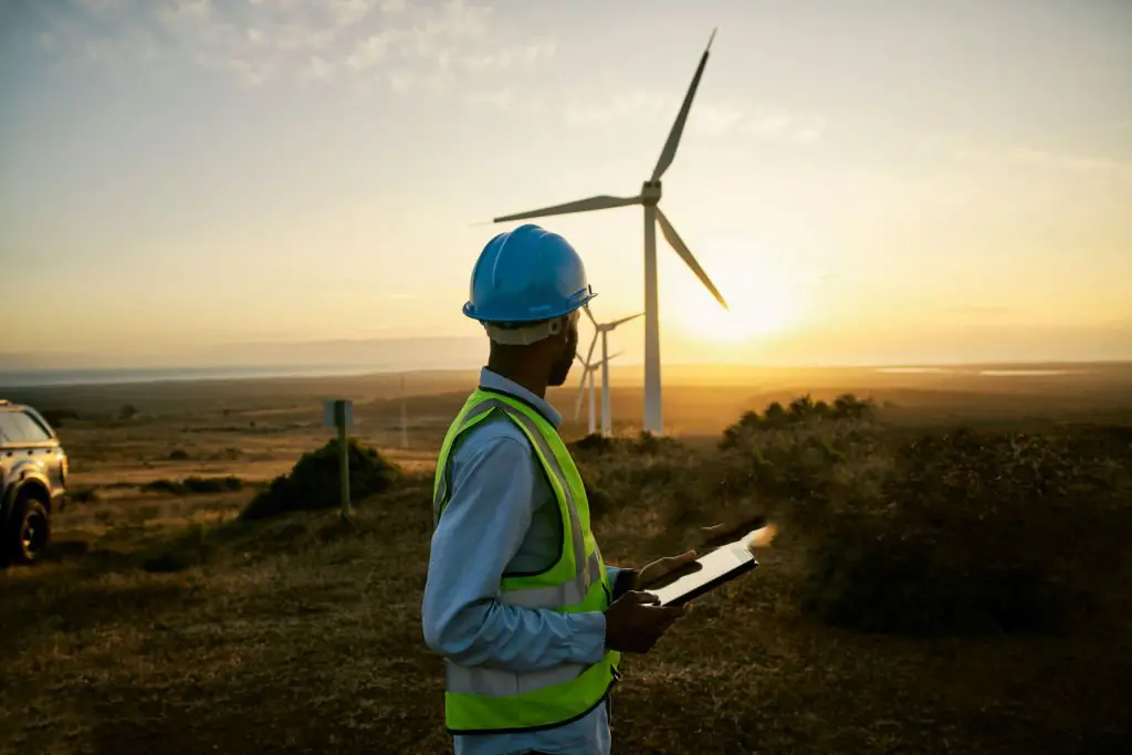 Un ingénieur avec une tablette devant des éoliennes au coucher du soleil, pour l'énergie propre, l'électricité et l'innovation écologique
